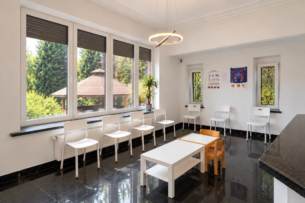 Salle d'attente vue sous un autre angle : chaises, tables basses et fenêtres sur le jardin